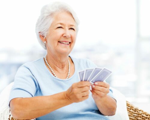 Happy senior woman playing cards while looking away at home. Horizontal shot.